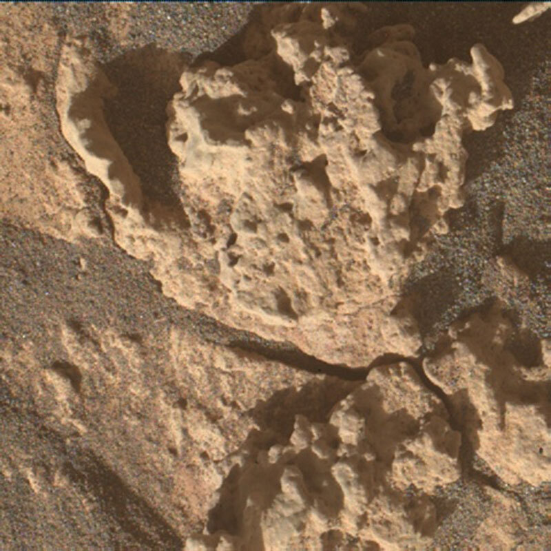 This is a colored image of the sandy, rocky surface of Mars. There are some large textured rocks with light shinning on them. The rough texture of the rock is emhpasized by tiny shadows on the rock. The large rocks are on a grainy sand-like surface.