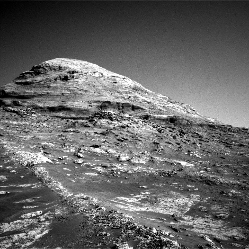 The Curiosity rover took this black and white image of a hill with rocks on the surface of Mars.
