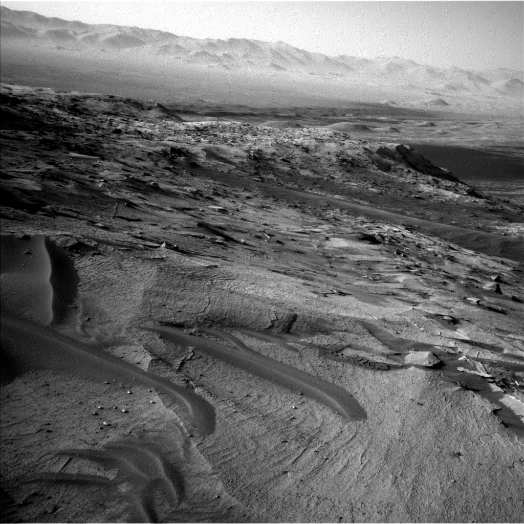 This is a black and white image of low, sandy hills. There are higher hills in the horizon.
