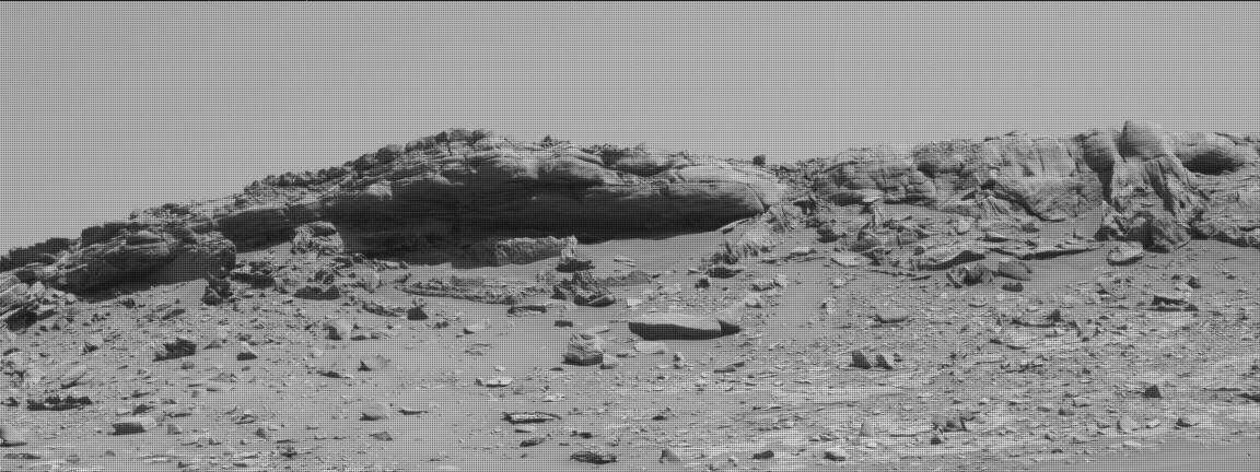 This is an image of two sized large boulders that appear as low hills. The surface is sandy with lots of smaller rocks. There is a clear sky in the background.