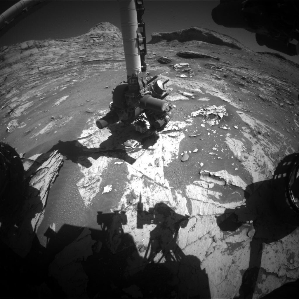 A black and white image of Curiosity's arm touching the surface of Mars.