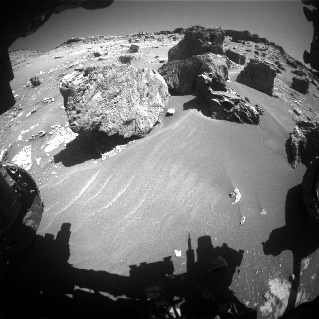This is a black and white image of large boulders, low hills and smooth sand on Mars.