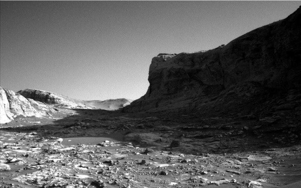 This is a black and white image of the rocky surface on Mars. A large hill is present in the background.