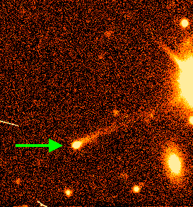 Primer plano de un cometa en un cielo nocturno estrellado.  El cometa está ubicado en el cuadrante inferior derecho y es brillante con una cola alargada prominente que se extiende diagonalmente hacia la parte superior izquierda, indicada por una superposición de una flecha verde que apunta en la dirección de la cola.  El fondo es un denso mosaico de estrellas, y hay un gran orbe sobreexpuesto en la esquina superior derecha, bañando parte de la imagen con su brillo.