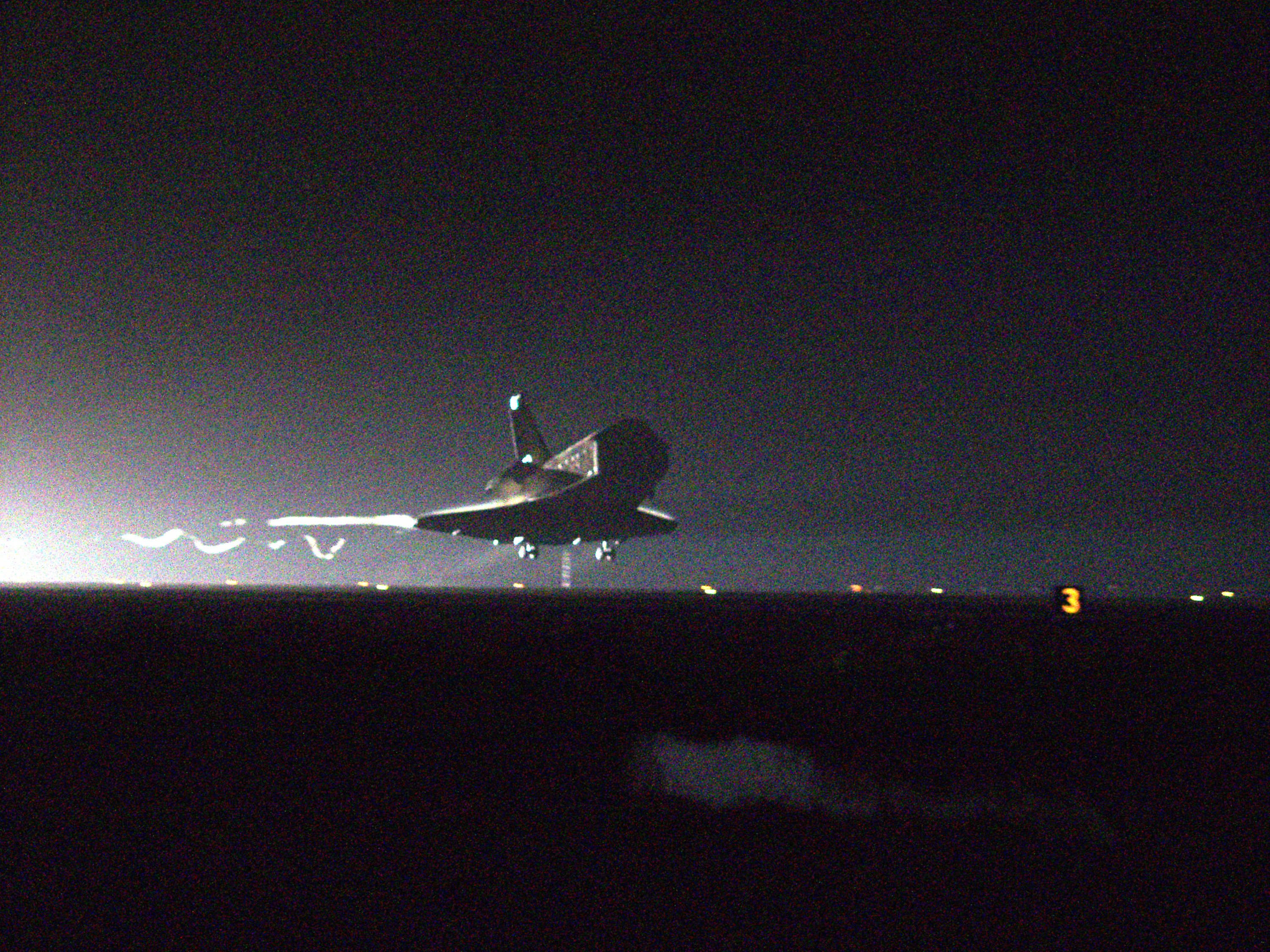 The space shuttle columbia is dimly seen from the front coming in for a landing in the early morning darkness.