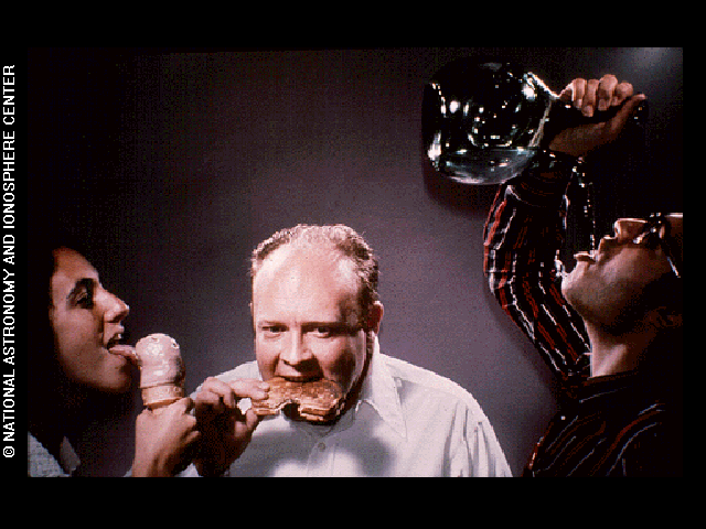 A woman licks an ice cream cone next to a man biting a sandwich, while a third person pours water from a glass pitcher into their mouth