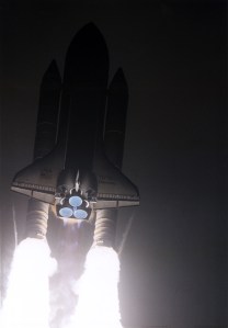 Seen mostly in shadow with engines blazing white gouts of fire, Discovery rises into the dark sky.