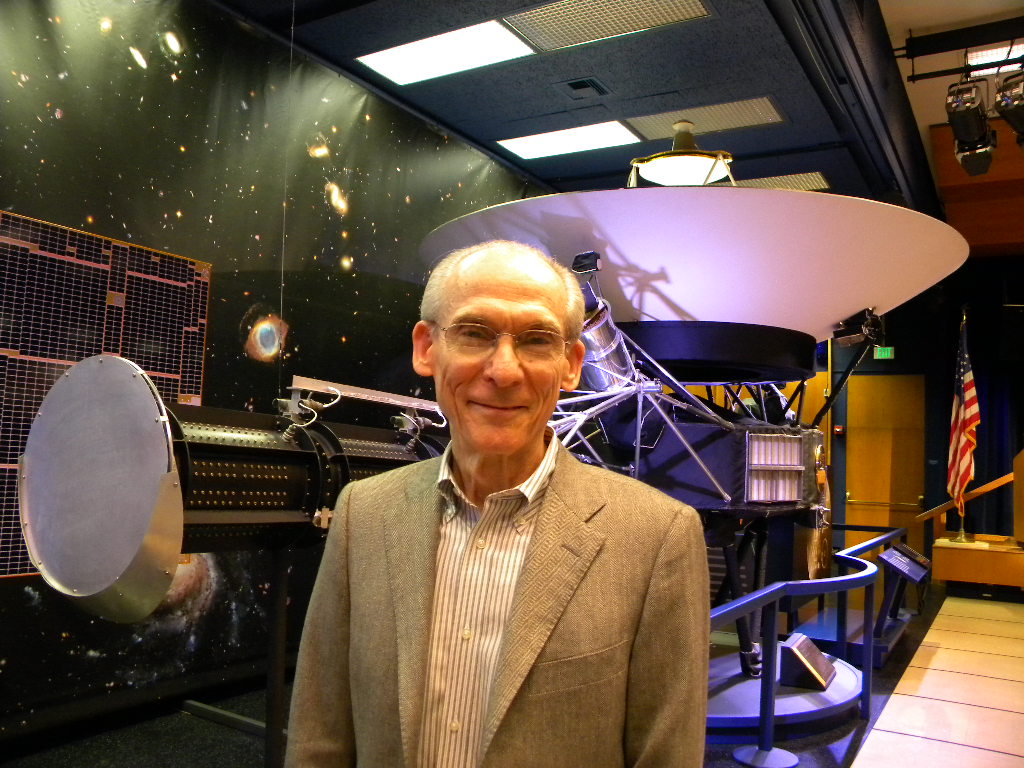 A smiling man in a sports jacket is standing in front of a full-size Voyager model.