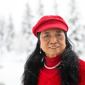 Portrait photo of a woman with long dark black hair wearing a red hat and matching red sweater which contrasts with the snowy white background.