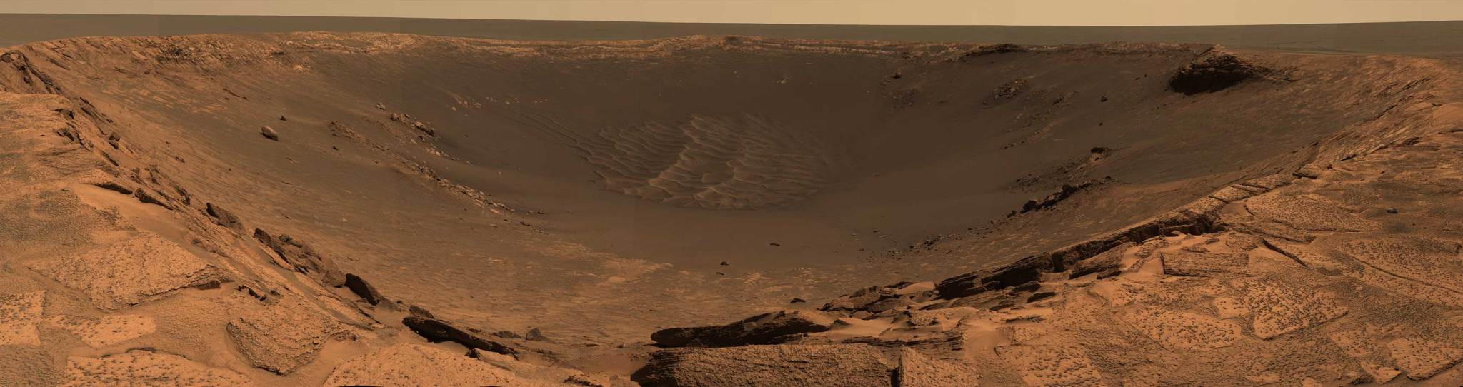 A wide panorama of Mars shows the rim of a vast crater.