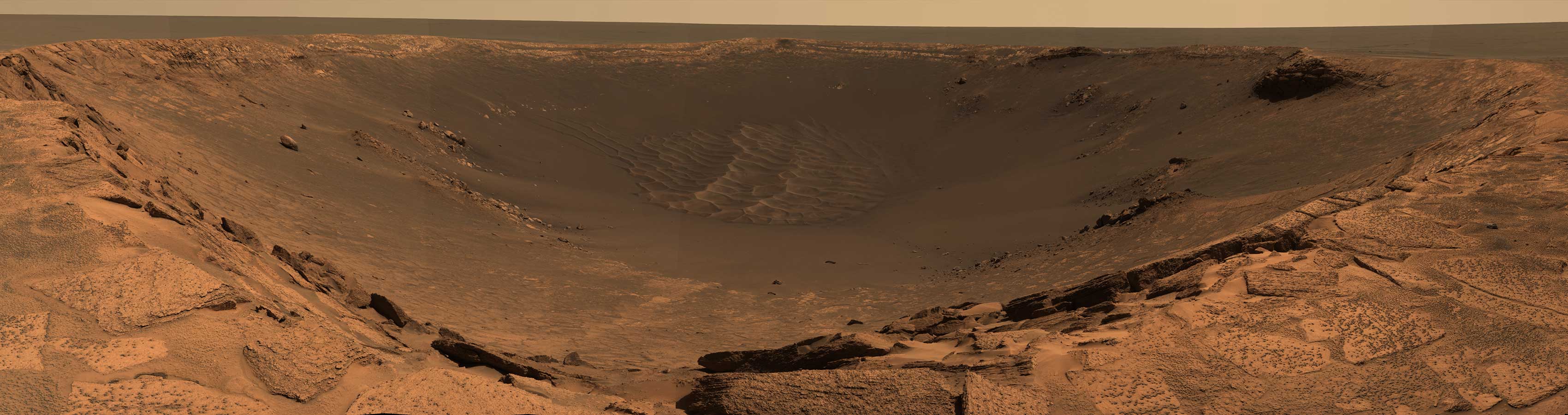 A wide panorama of Mars shows the rim of a vast crater.