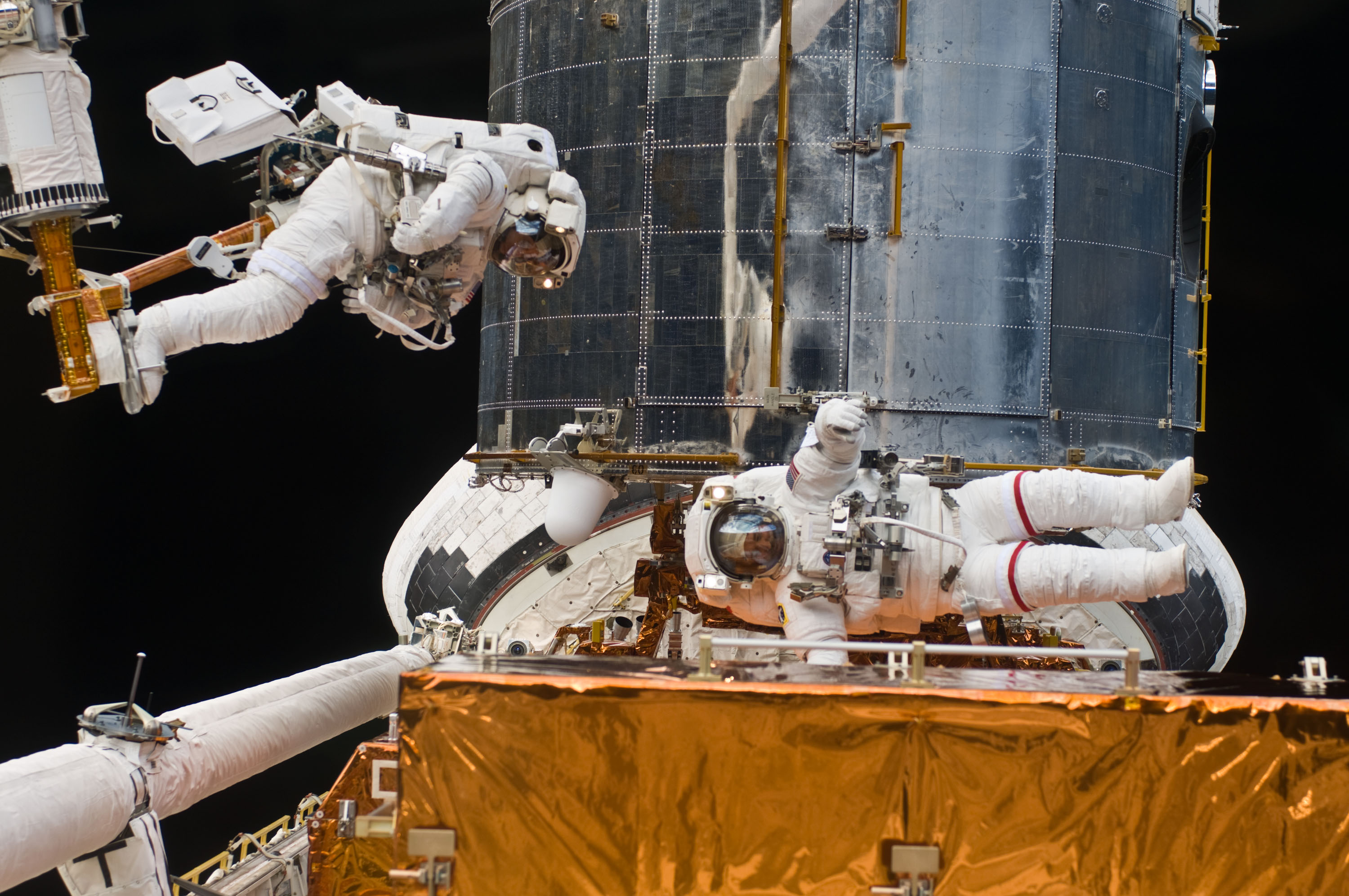 One astronaut working on Hubble floats on his side, another is attached by his feet to the shuttle's robotic arm.