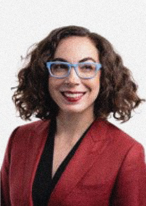 Erika Hamden headshot, female, brown wavy short hair, blue glasses, red blazer, smile.