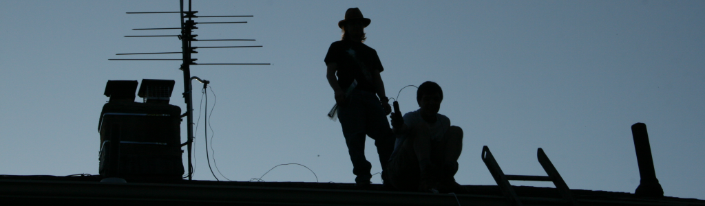 A silhouette of two people on a roof with ham radio equipment