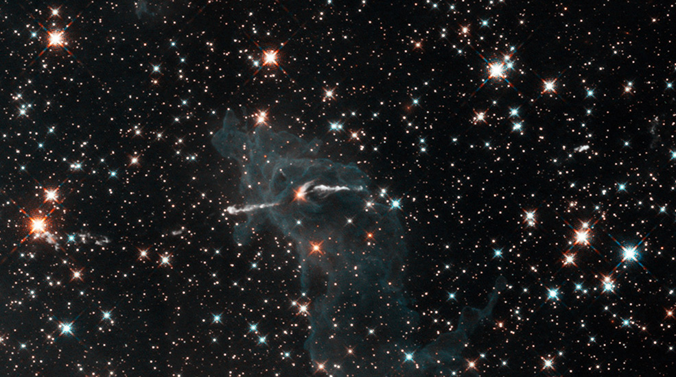 The column of gas and dust is a dim, ghostly gray version of itself and mostly transparent. Stars can be seen through it and a cloudy jet of gas is visible emerging horizontally from within the column. The background is black space dotted with a myriad of stars.