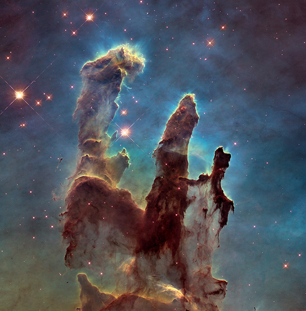 Three giant pillars of rusty colored dust and gas with a blueish green background.
