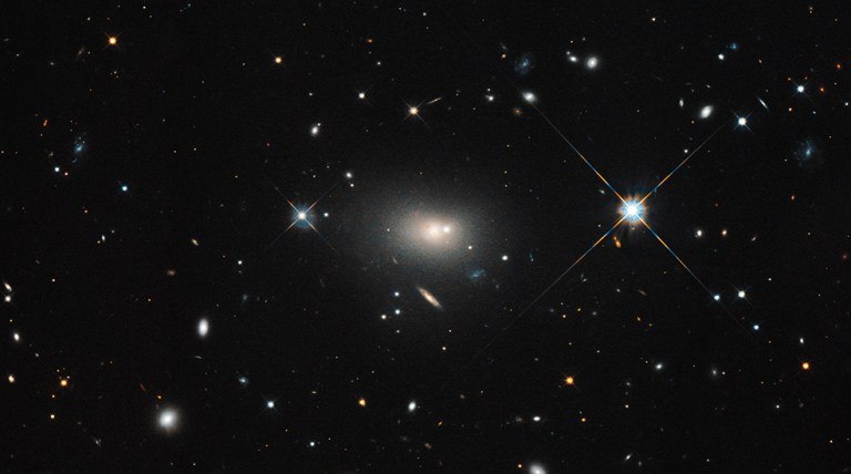 Black space with multiple galaxies visible, large white glowing supermassive black hole in the center and two bright stars on each side.