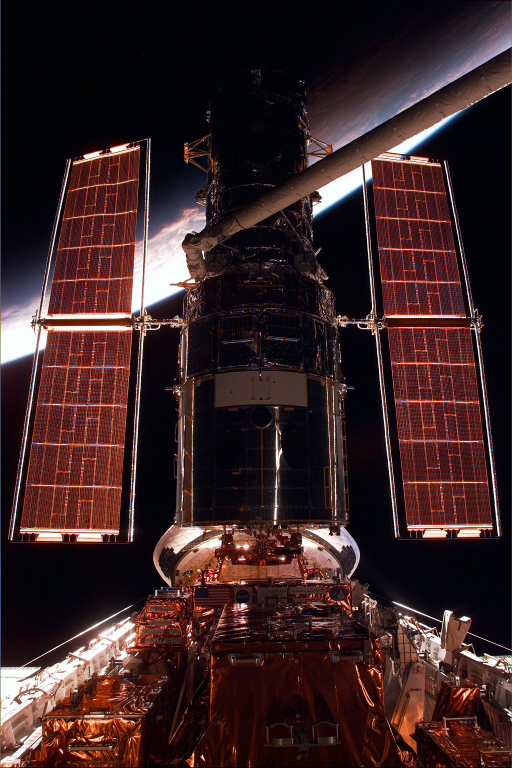 The blue edge of Earth forms a backdrop for a backlit Hubble in Discovery's cargo bay.