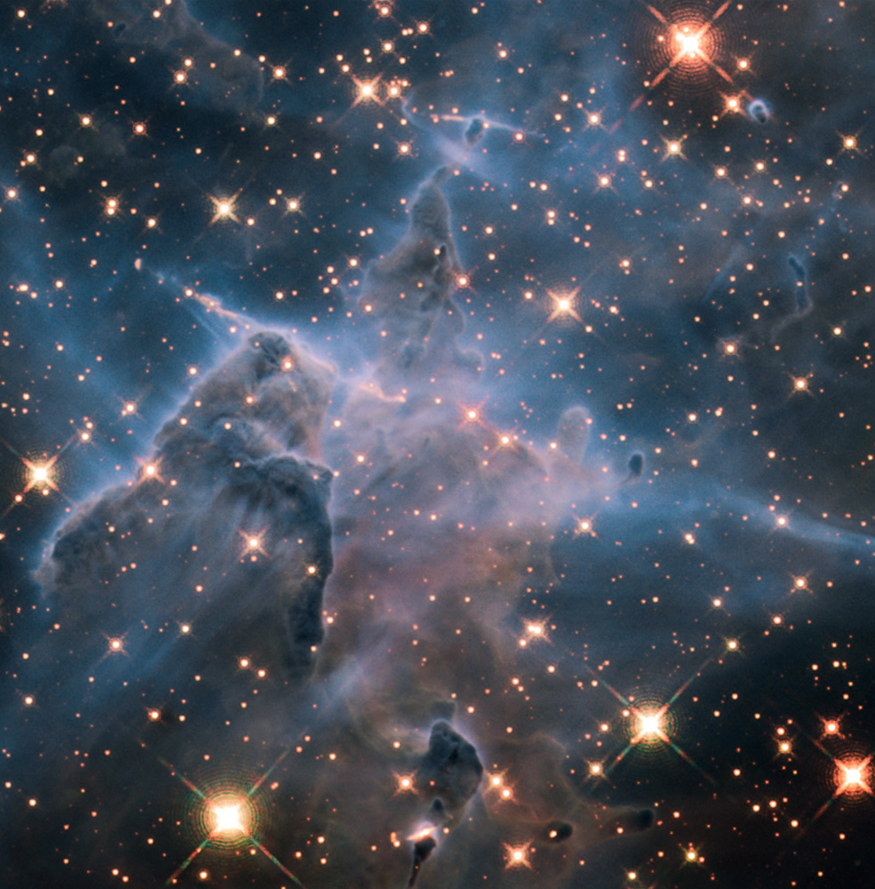 This near-infrared image shows a myriad of stars behind the gaseous veil of the nebula's background wall of hydrogen, laced with dust. The foreground pillar becomes semi-transparent because infrared light from the background stars penetrates through much of the dust. A few stars inside the pillar also become visible.