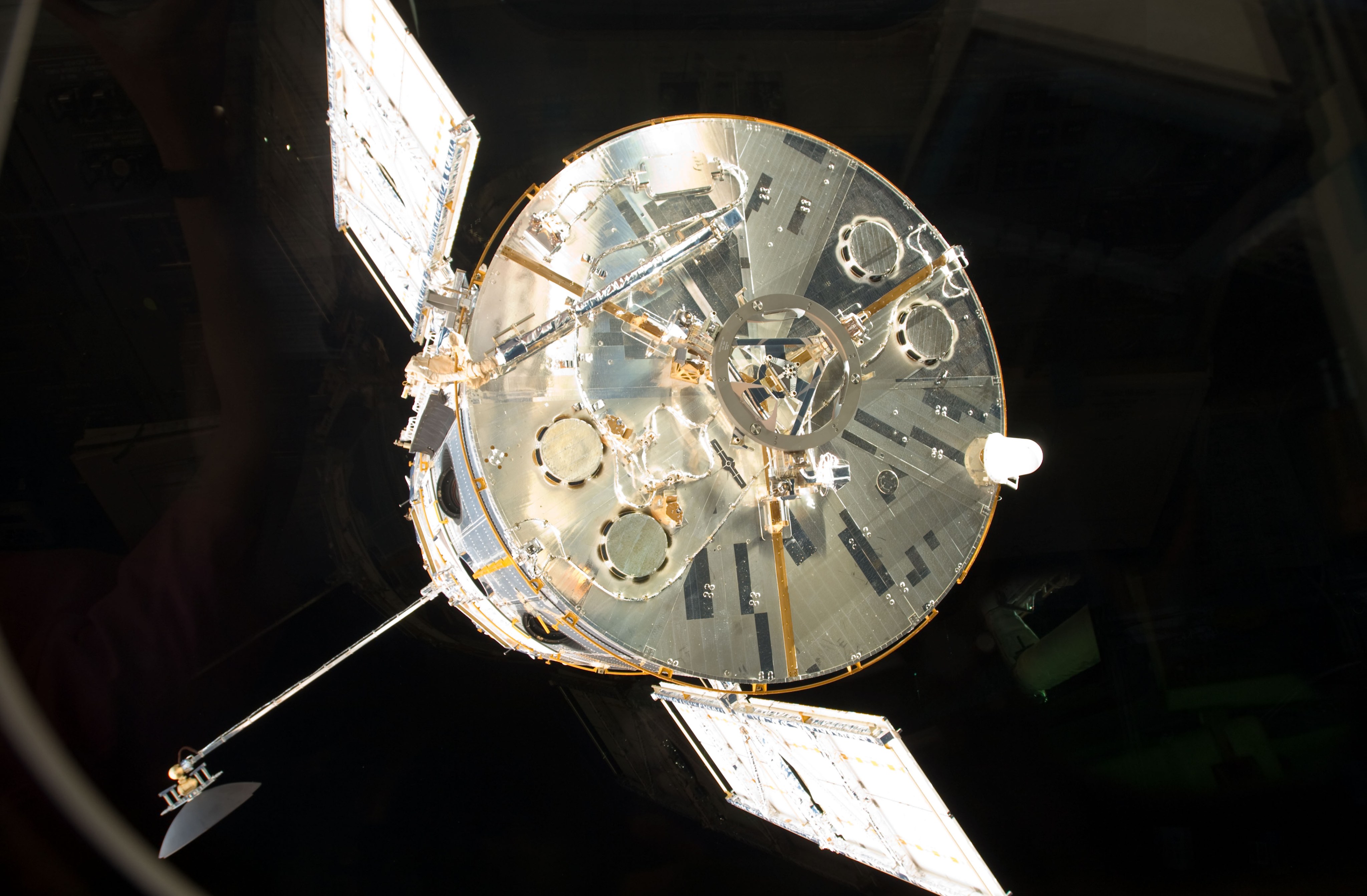 Hubble is seen through a window floating away into the darkness of space after being released by the space shuttle. Hubble's solar panels, antennae and underside are all visible.