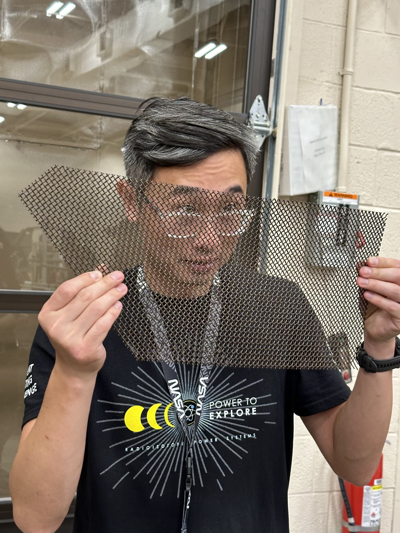 A man peers through a sheet of mesh while talking to students.