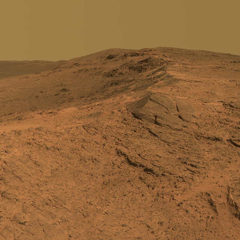 The rim of a large Martian crater rises in the foreground of this Martian landscape.