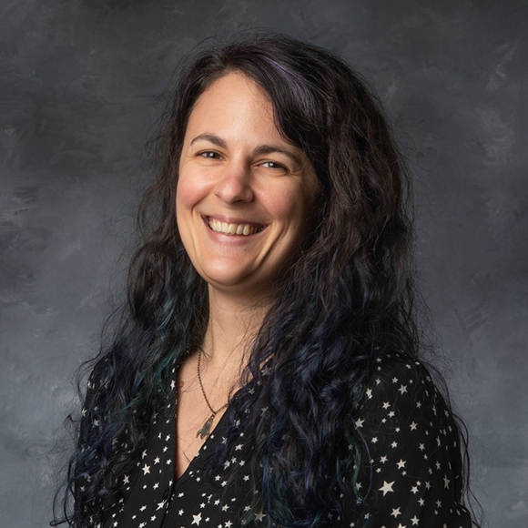 Keri Hoadley headshot, female, long black wavy hair, black printed shirt, smile.