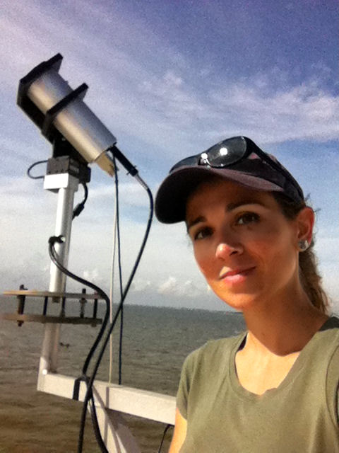 Portrait photo of a young woman outside standing next to a telescope.