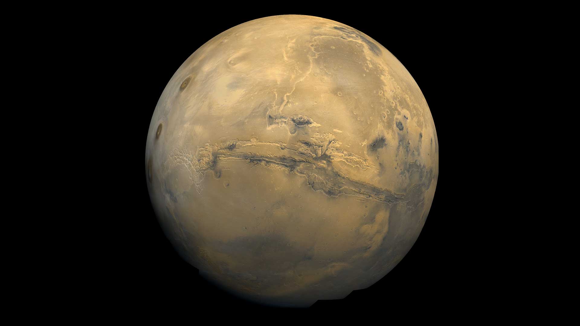 Mars is a reddish brown in this image from a spacecraft. A deep gash is visible across the center of the planet.