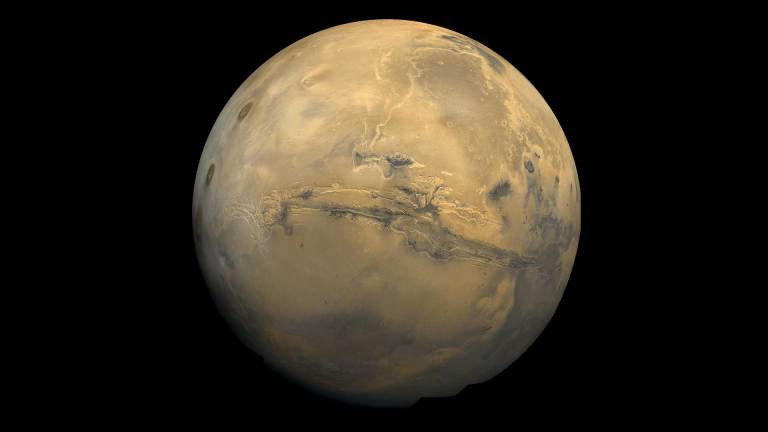 Mars is a reddish brown in this image from a spacecraft. A deep gash is visible across the center of the planet.