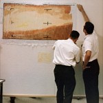 Two men color in data on strips of paper mounted to a wall.