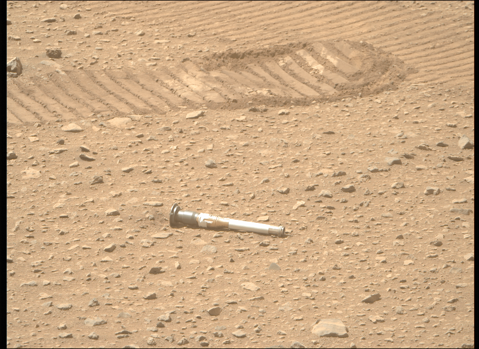 Perseverance takes a photo of one of a sample tube on the Martian terrain.