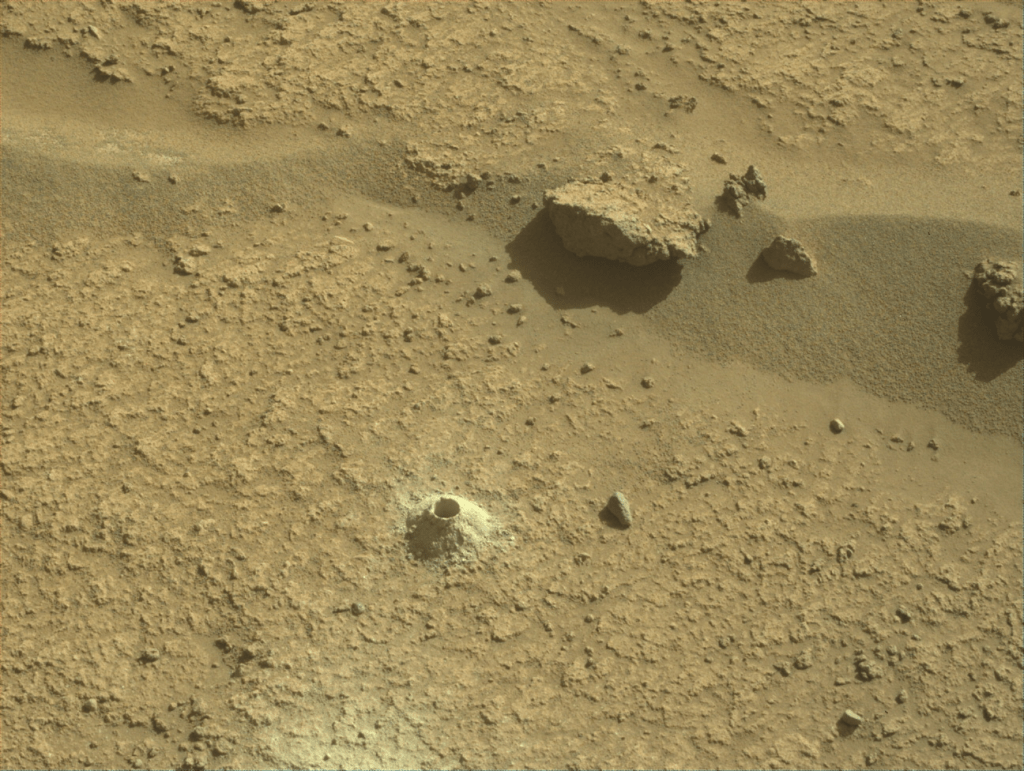 Image taken was taken by the Mars Perseverance rover after collecting the rock sample 21 at Pilot Mountain. There is a drill hole of where the sample was collected along with a few rocks surrounding the area.