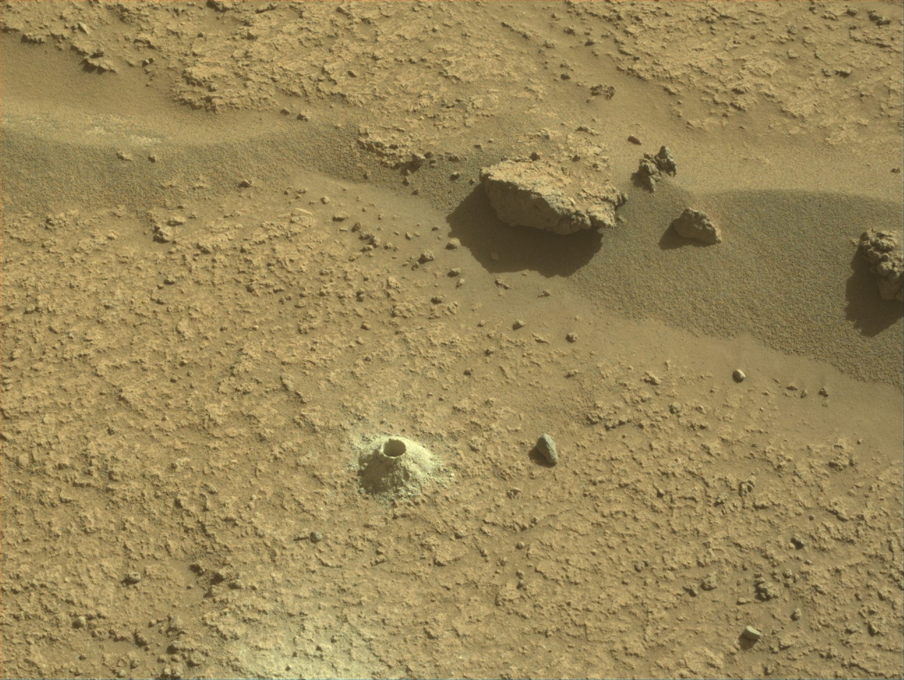 Image taken was taken by the Mars Perseverance rover after collecting the rock sample 21 at Pilot Mountain. There is a drill hole of where the sample was collected along with a few rocks surrounding the area.