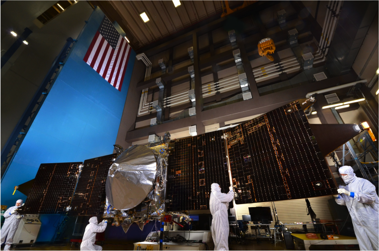 Four men in cleanroom suits work on the MAVEN spacecraft, which has its solar arrays fully spread.
