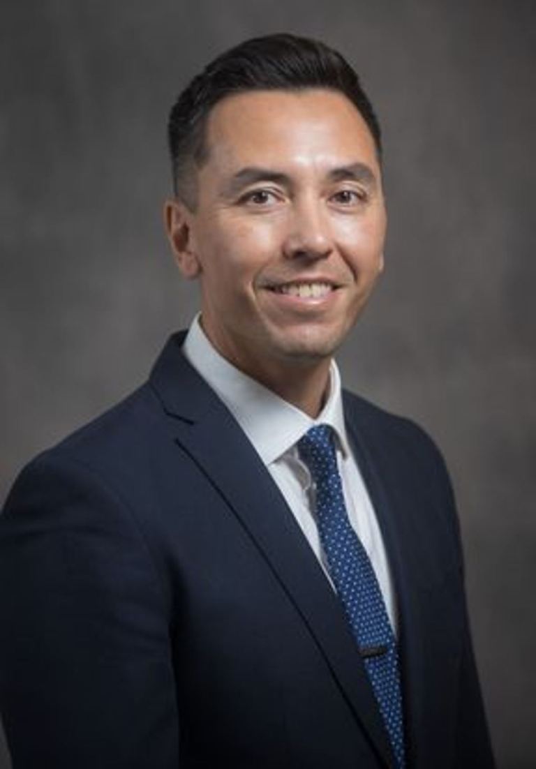 Half body portrait of Randy McEntaffer in a black suite and blue tie, clean shaven, tight haircut with black hair, natural smile.