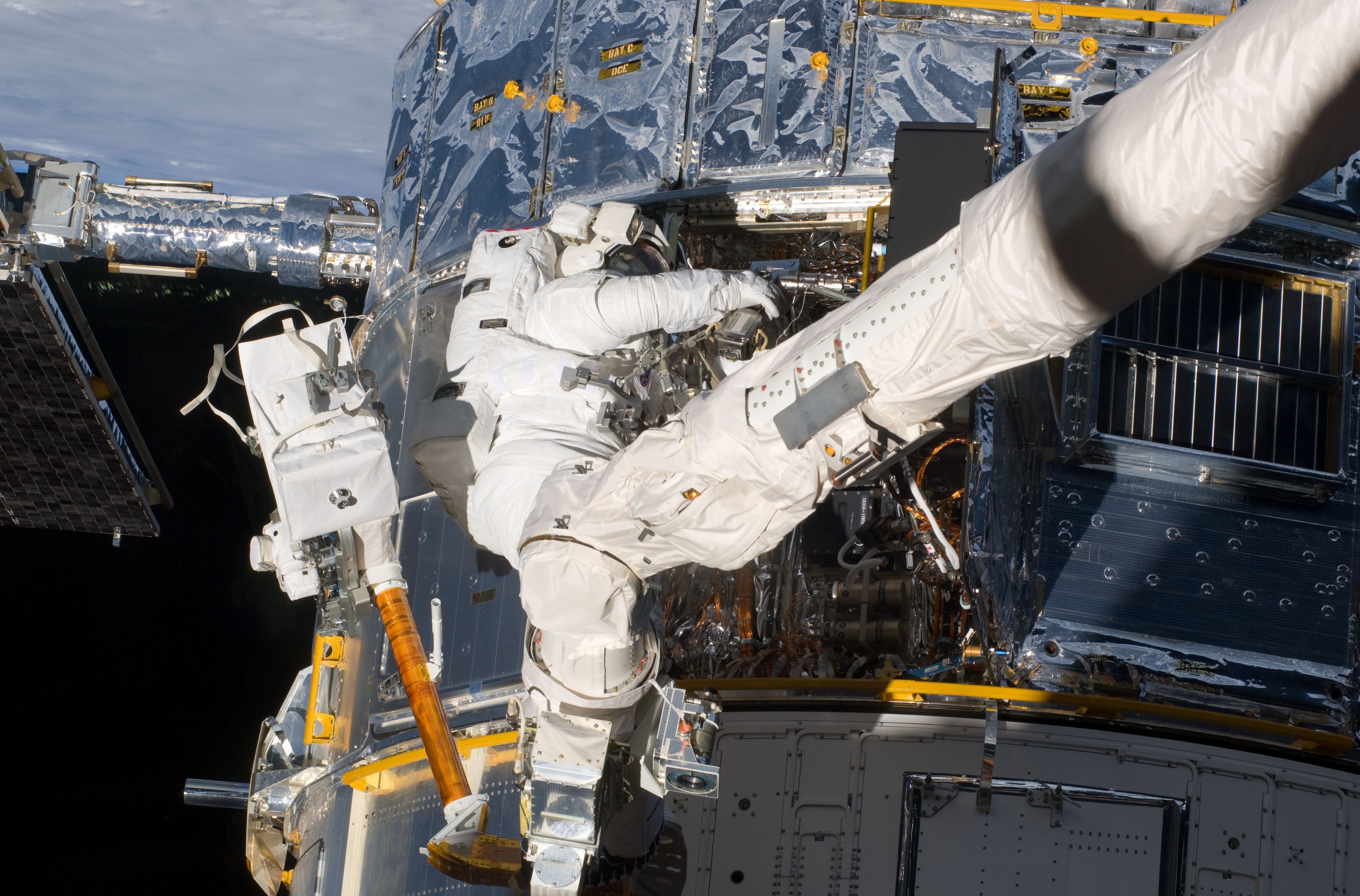 An astronaut is partially obscured by the bulk of the space shuttle's robotic arm as he works on the innards of the Hubble telescope.