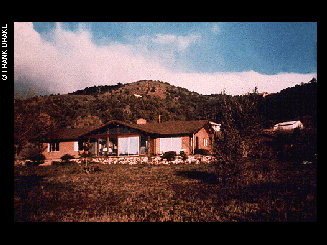 A mid-20th-century ranch-style single-story house in a desert grasslands area, positioned in front of a large hill