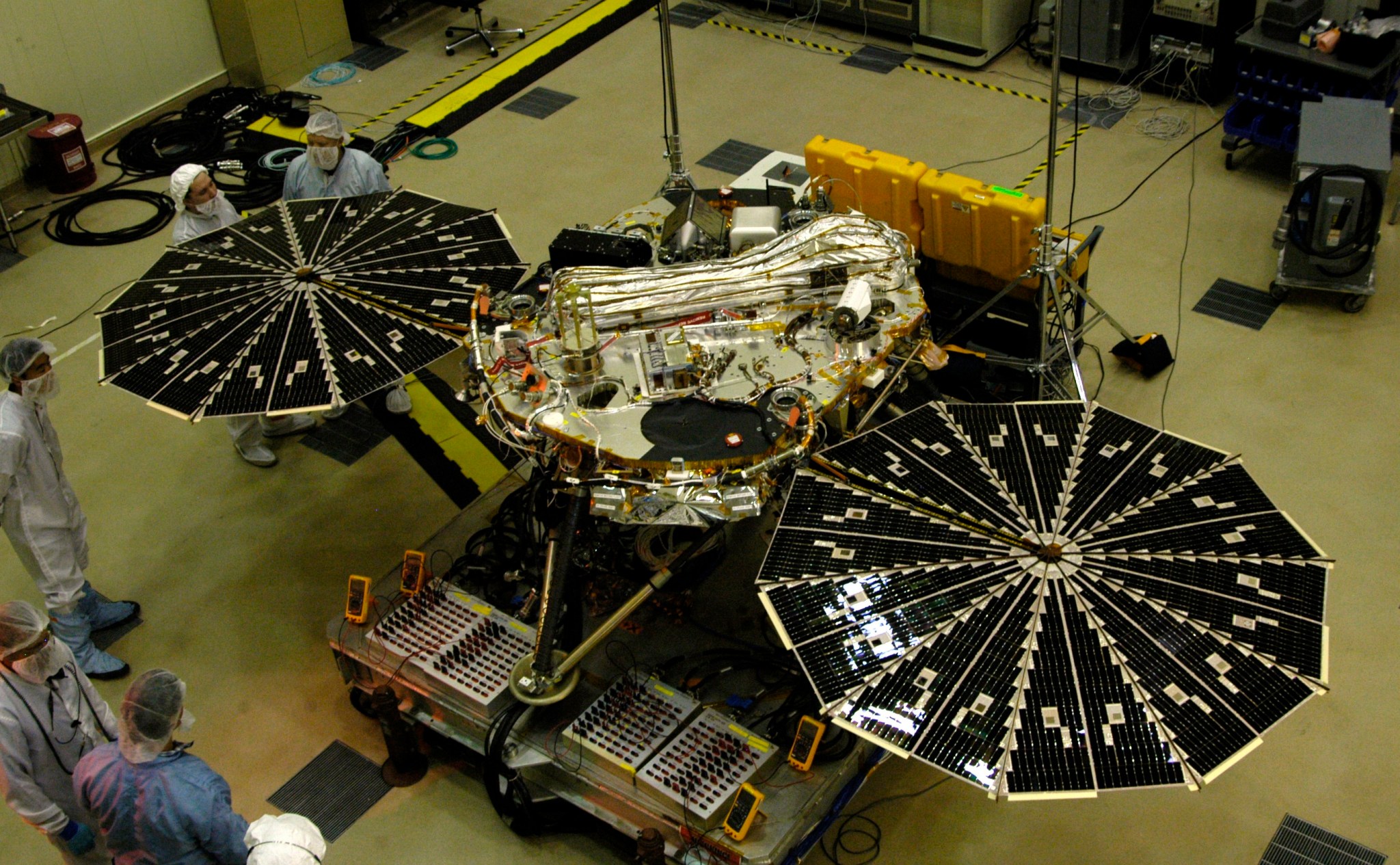 A four-legged spacecraft is sitting in a cleanroom with its solar panels wide open.