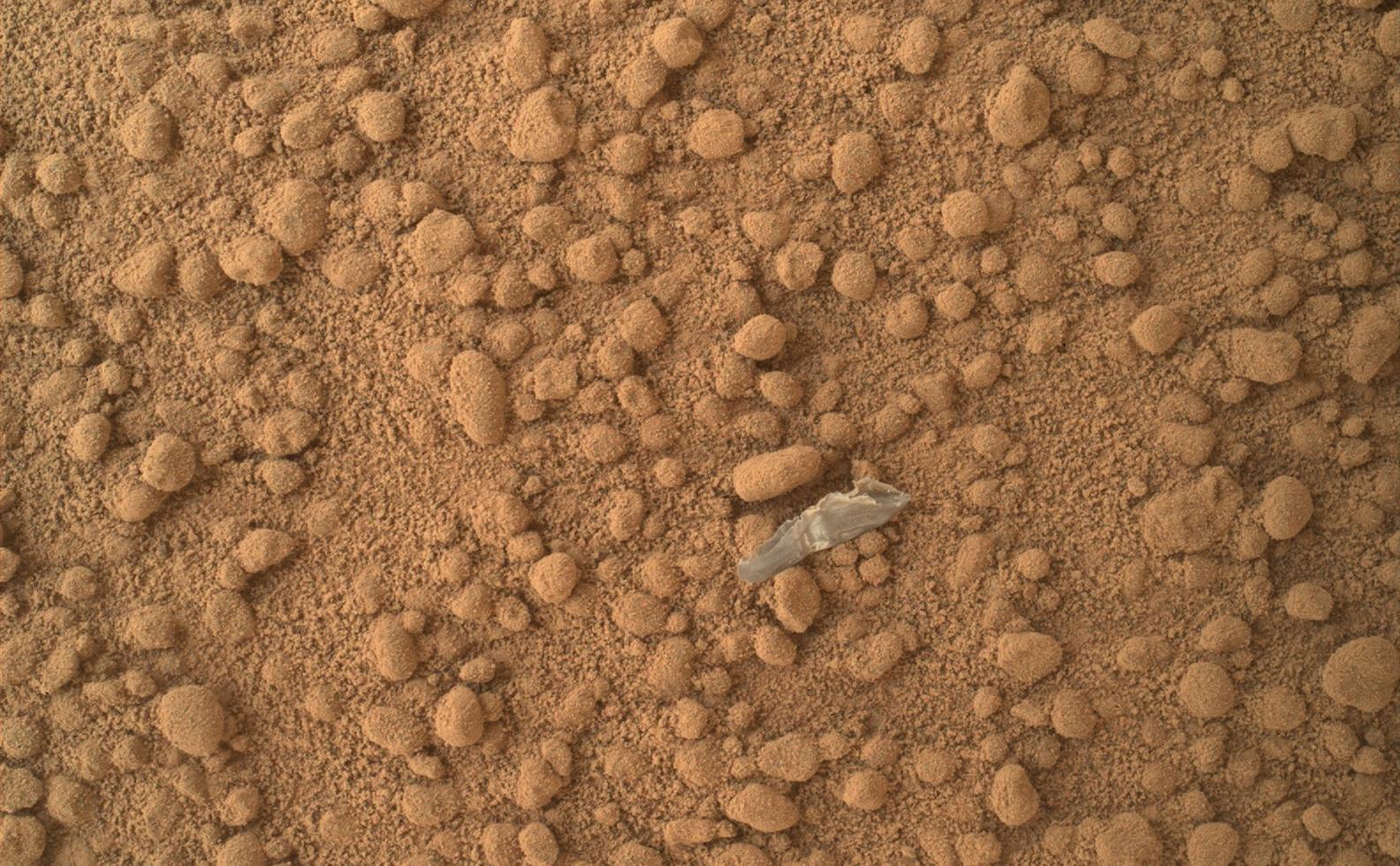 This image from the Mars Hand Lens Imager (MAHLI) camera on NASA's Mars rover Curiosity shows a small bright object on the ground beside the rover at the "Rocknest" site.