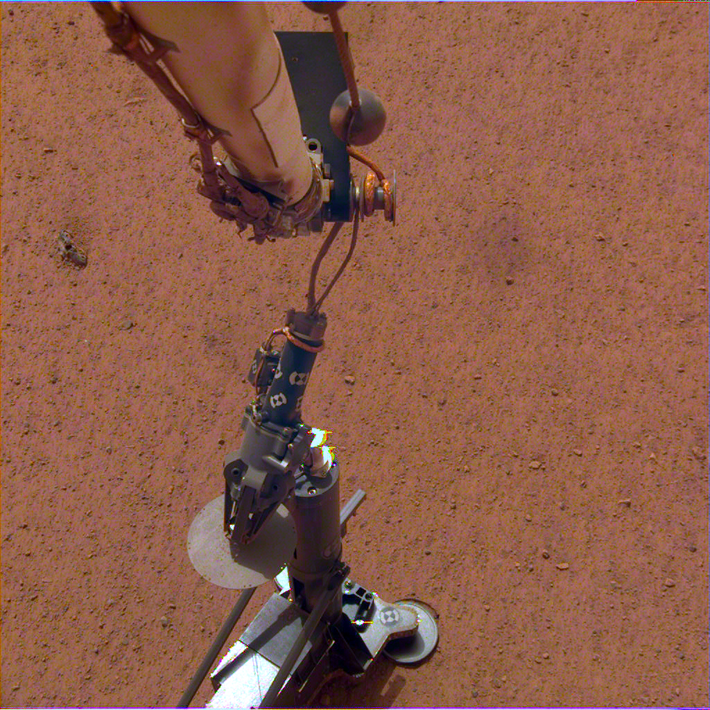 Two pieces of cylindrical science equipment are stacked on the flat red surface of Mars.