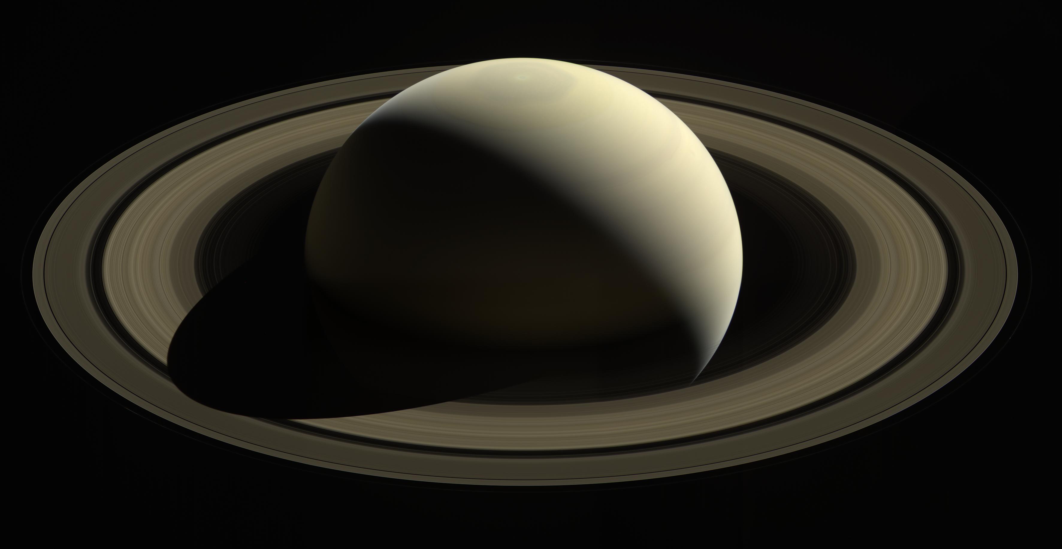 A spacecraft looks down on a soft gold-colored Saturn surrounded by its rings.