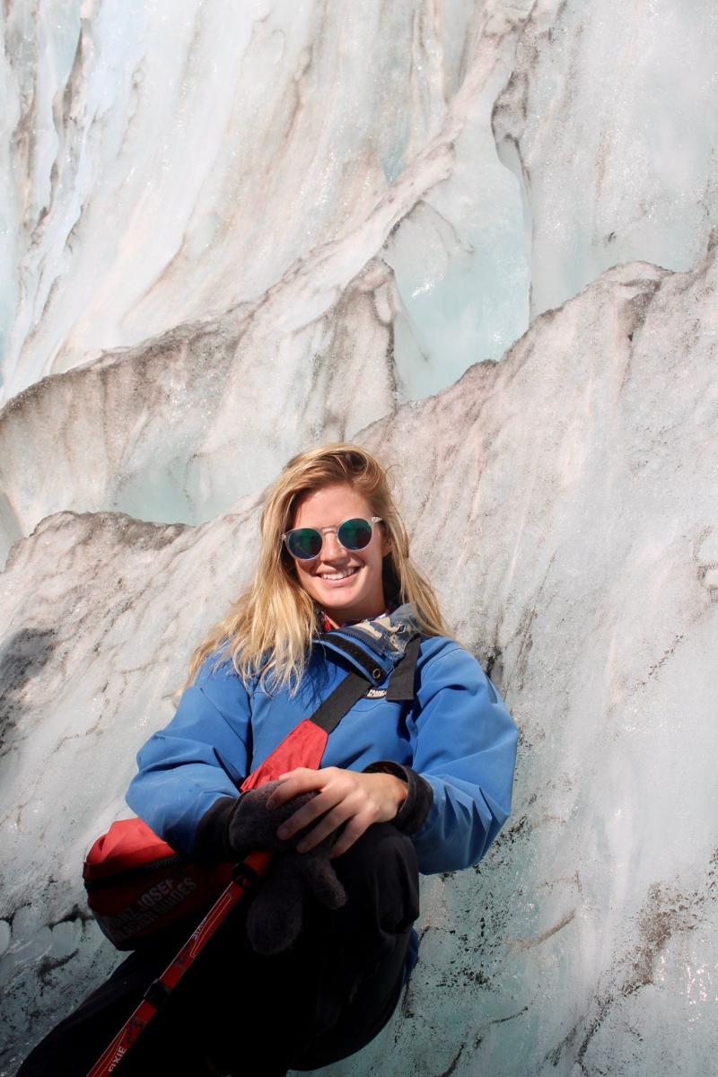 Photo of a woman in sunglasses and a blue winter jacket sitting against a rocky background.