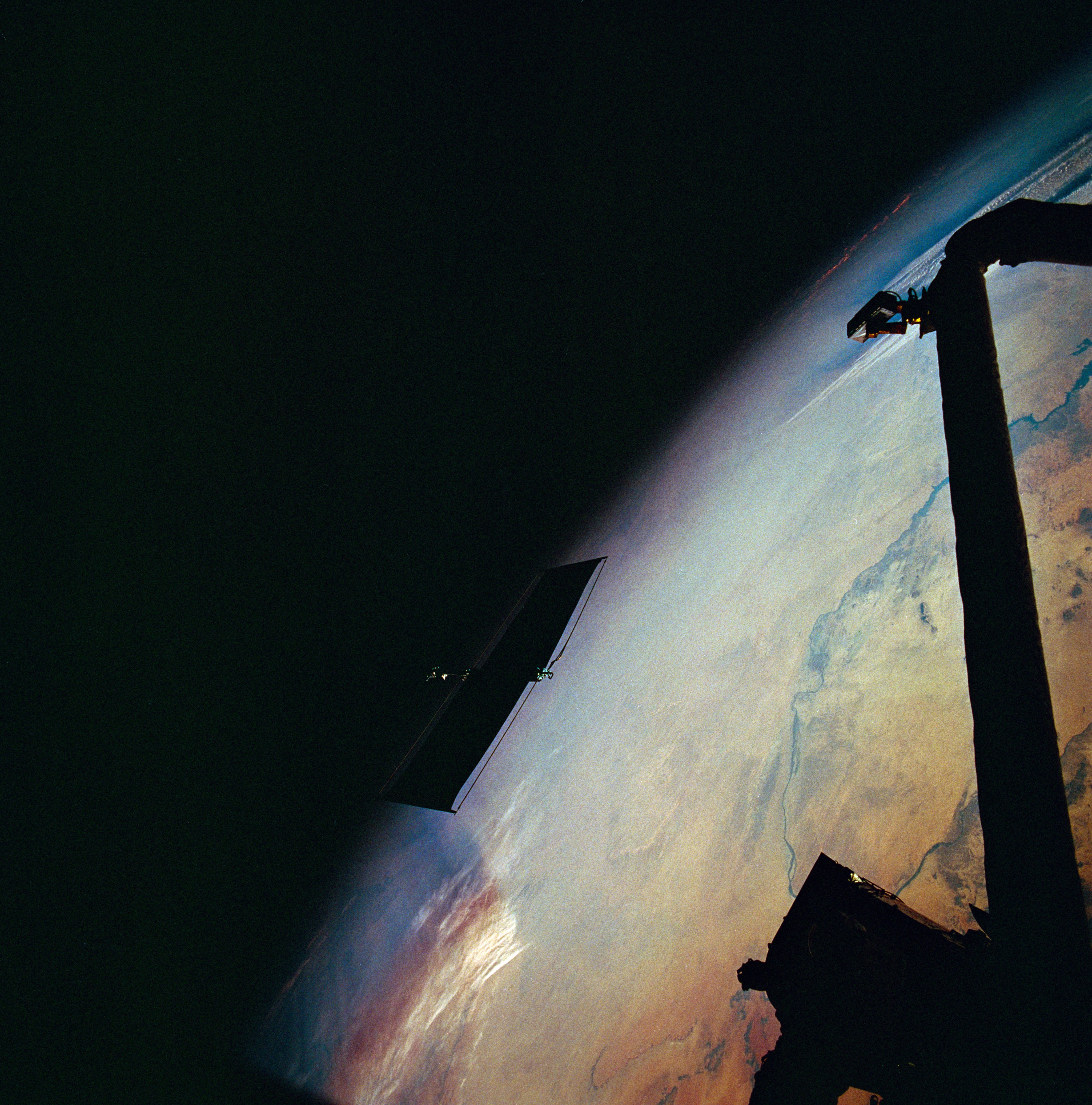 A solar panel, seen almost entirely in shadow, floats away against the backdrop of Earth.