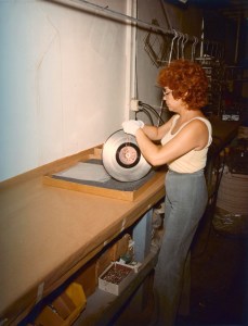 A woman attaches a wire loop to the Voyager Golden Record for dipping into a chemical vat.