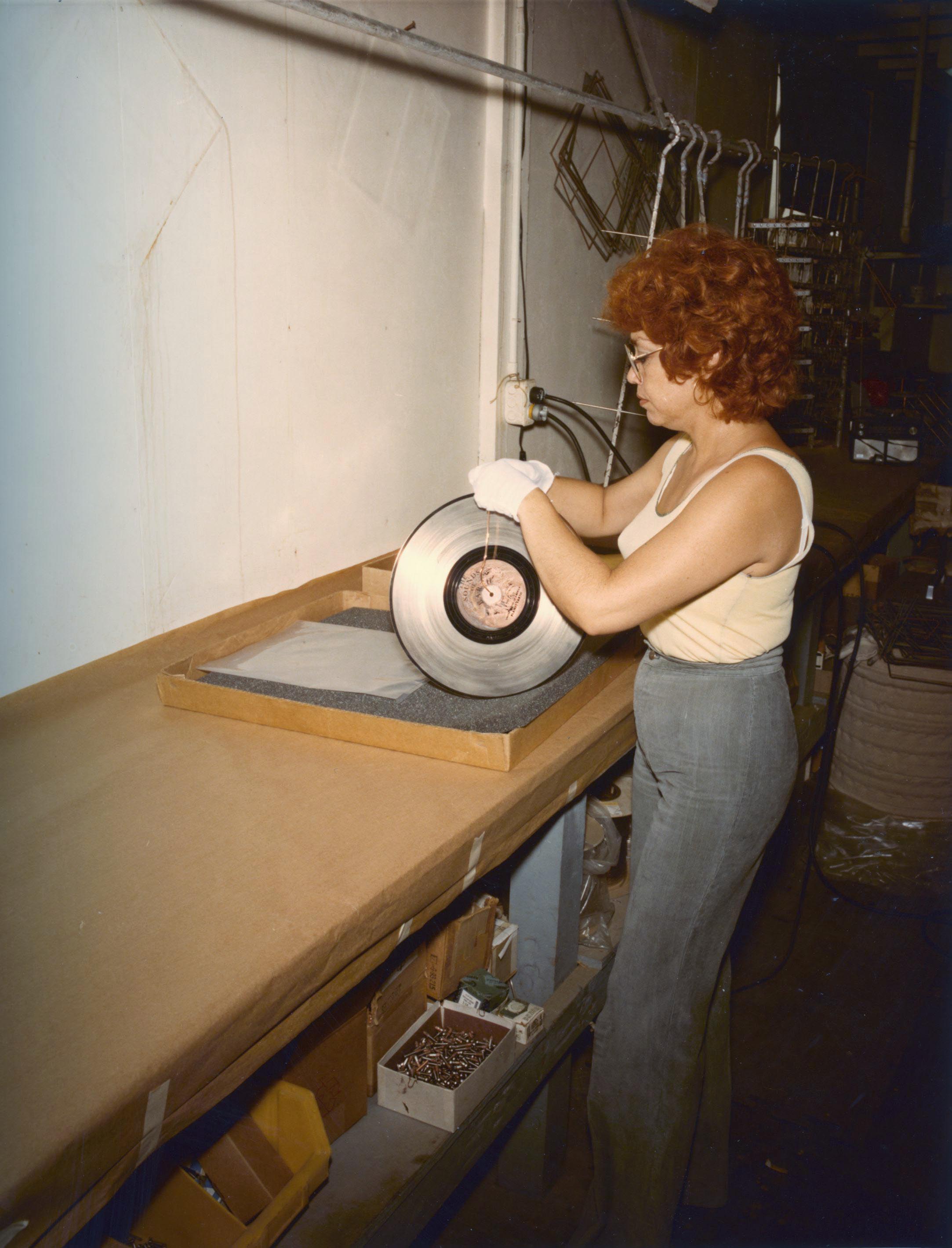 A woman attaches a wire loop to the Voyager Golden Record for dipping into a chemical vat.