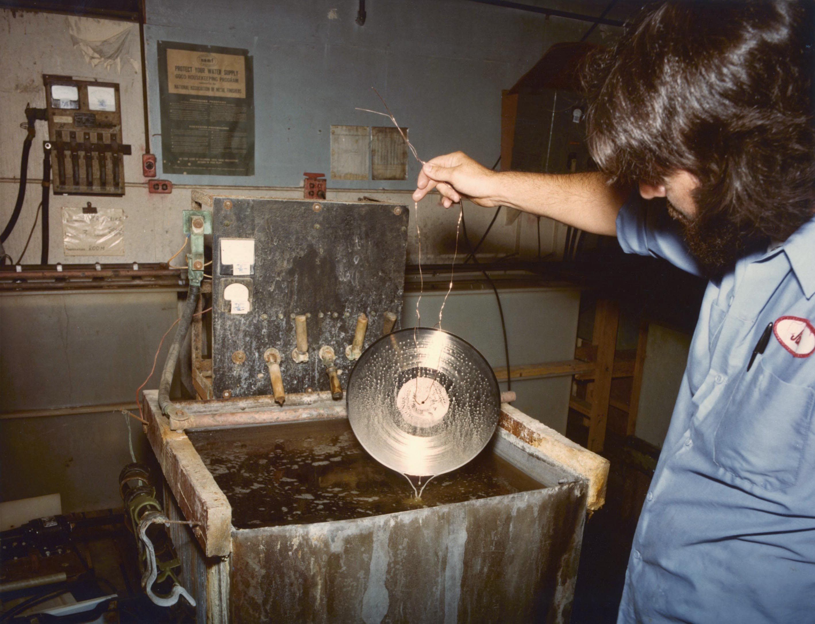 A man dips the golden record into a sink-sized vat of chemicals.