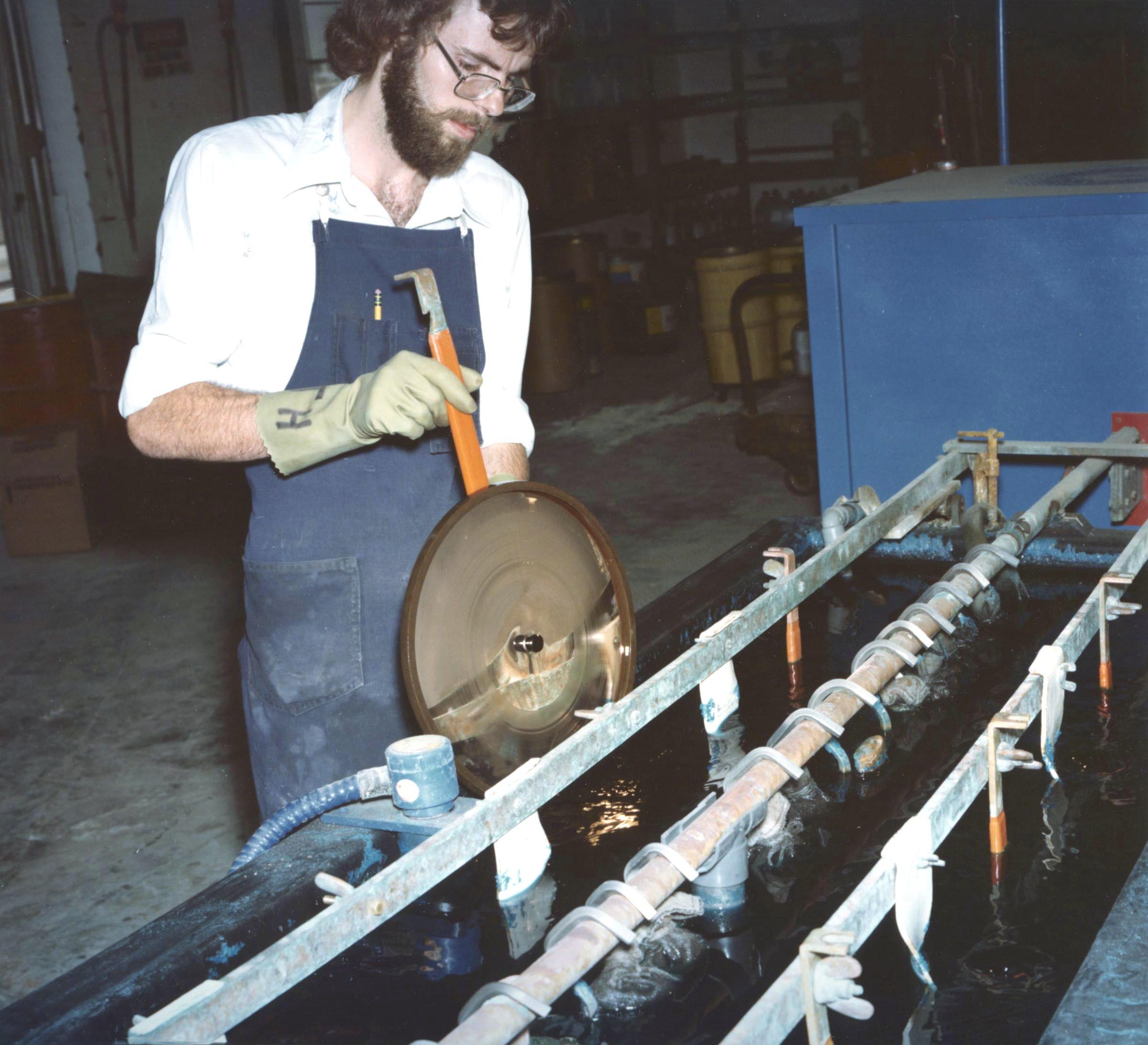 A man guides a golden record through a manufacturing process.