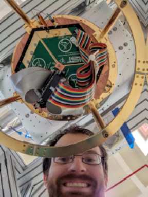 A selfie of Jordan Wheeler with a cryogenic detector array hooked up to an LED pixel mapper circuit board all installed in a cryostat.