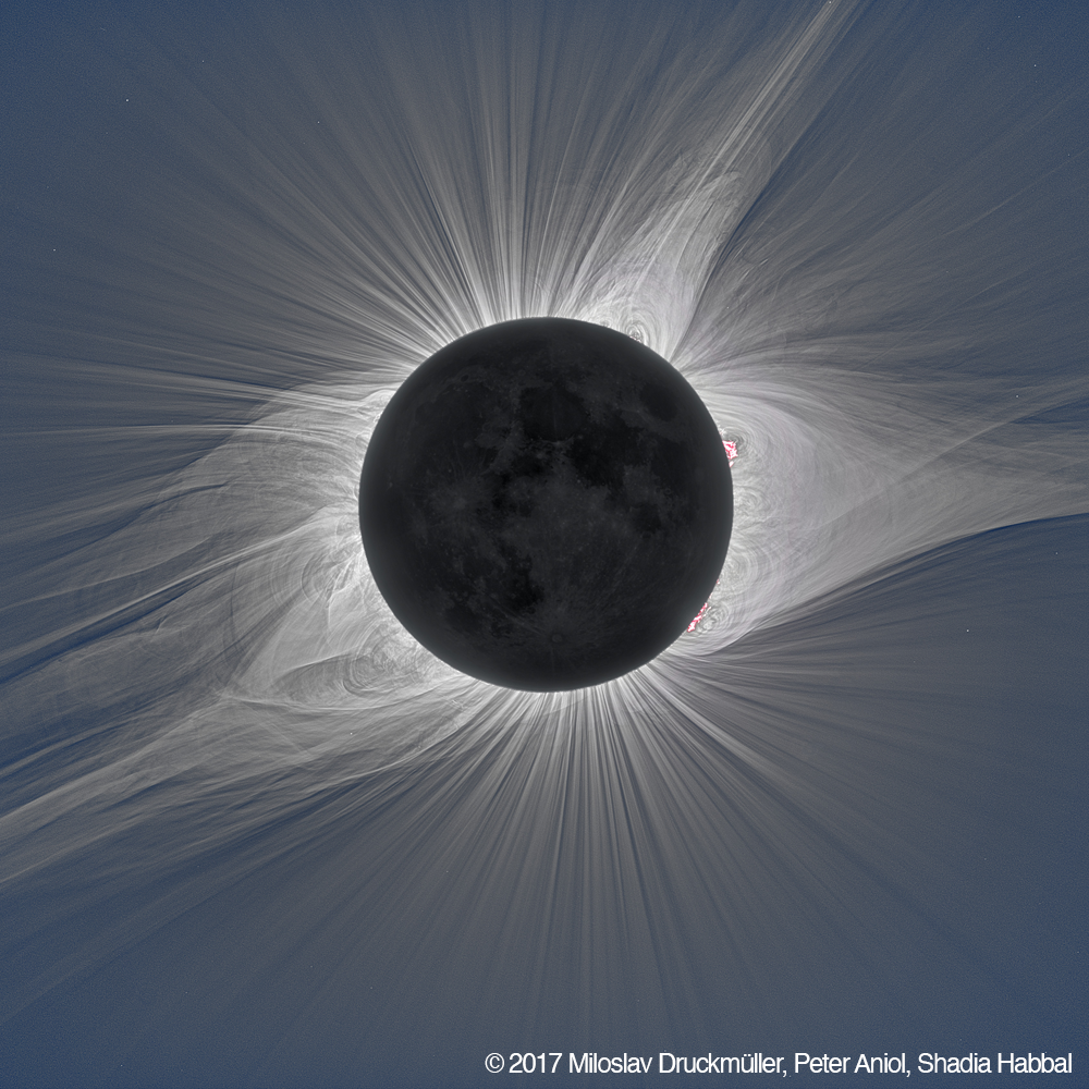 A processed image of the total solar eclipse from 2017 shows the moon completely covering the disk of the Sun. Encircling the moon, the solar corona can be seen in white light with well-defined structures.